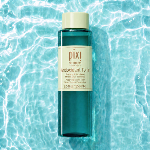 Pixi Skintreats Antioxidant Tonic in a translucent teal bottle with a cream-colored cap and label, centered against a background of rippling turquoise water. view 1