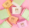 Pixi On-the-Glow SuperGlow cream products in pastel shades arranged in a circular flat-lay pattern on a solid pink background.